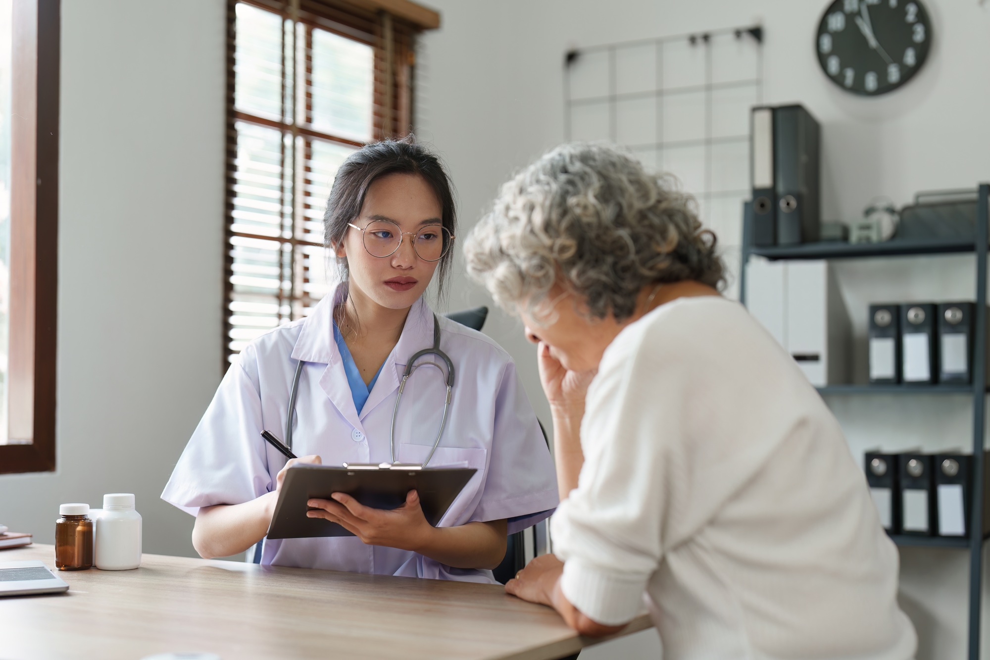 Doctor talking with elderly asian woman. Female primary care physician having conversation with