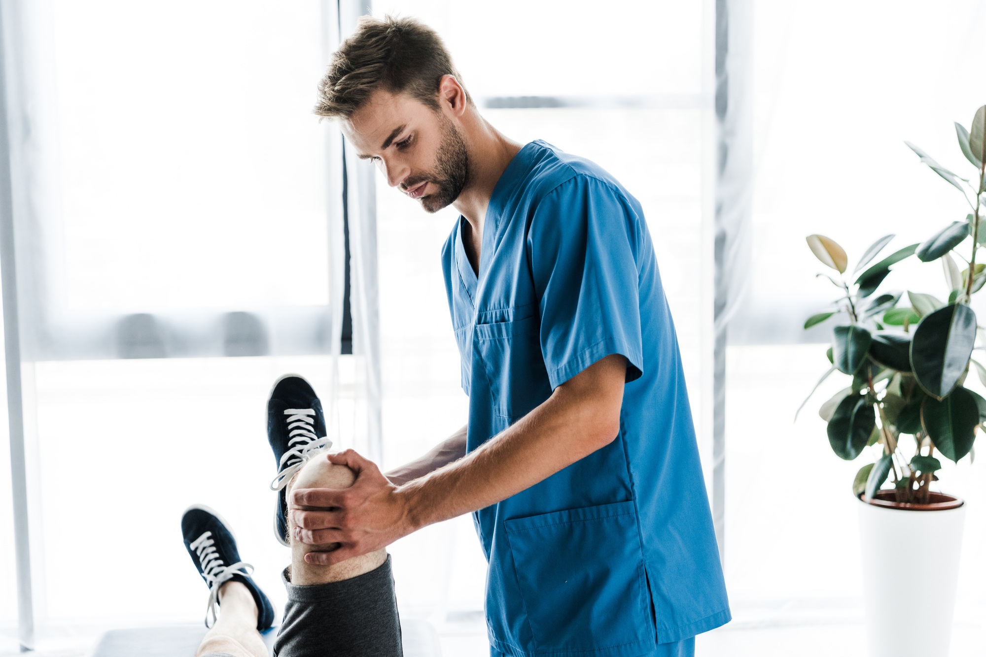 handsome doctor touching leg of mature patient